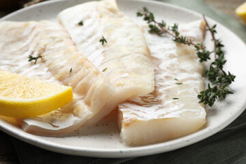 Fresh raw cod fillets with thyme and lemon on wooden table, closeup