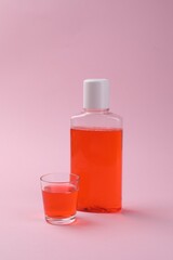 Fresh mouthwash in bottle and glass on pink background