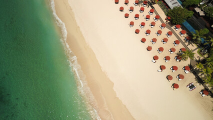 Top view of a beach club with swimming pool, sun loungers and red umbrellas on the white sandy ocean shore. White sandy beach, corals, turquoise water and a luxurious club on the coast of Bali.