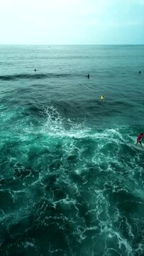 Vertical video aerial view of a young woman in a red swimsuit catching a wave. Sexy female surfer rides a wave on a surfboard and bounces. Women in extreme sports.