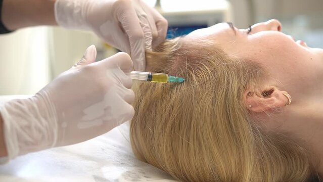 Cosmetologist makes a blond woman prp therapy against hair loss, injections in the scalp in a beauty salon. PRP for hair. The concept of cosmetology.