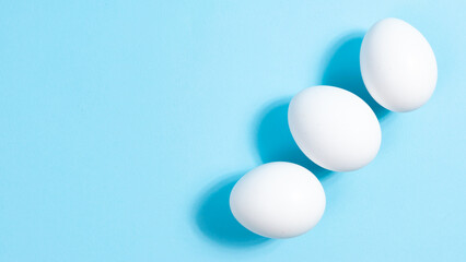 Three white chicken eggs on blue background. Minimal concept. concept of Easter or protein food. Close-up.