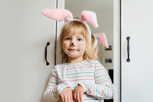 Smiling little girl with painted face and wearing bunny ears on Easter day. Preschool children spending time at home or daycare