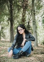 Naklejka na ściany i meble Beautiful latin american brunette woman with black hair, a black jacket and blue pants sitting on the grass