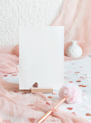 Vertical card near pink decorations, pen, hearts and tulle on white table close up, mockup