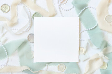 Card near light green and beige decorations and silk ribbons on white table top view, mockup