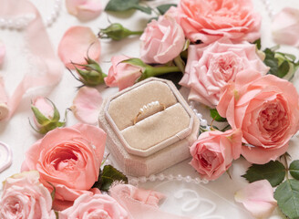 Engagement ring in a box between light pink roses and buds close up, wedding concept