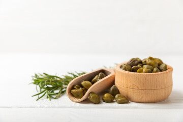 Capers in a bowl on a wooden kitchen table. Capers with sea salt and rosemary. Pickled capers.Mediterranean cuisine ingredient. Organic spices and seasonings. Copy space.