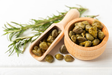 Capers in a bowl on a wooden kitchen table. Capers with sea salt and rosemary. Pickled capers.Mediterranean cuisine ingredient. Organic spices and seasonings. Copy space.