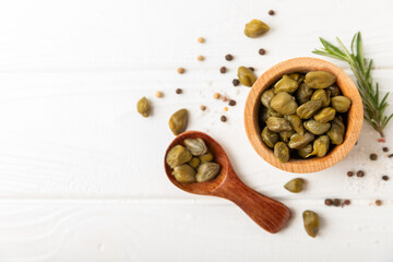Fototapeta na wymiar Capers in a bowl on a wooden kitchen table. Capers with sea salt and rosemary. Pickled capers.Mediterranean cuisine ingredient. Organic spices and seasonings. Copy space.