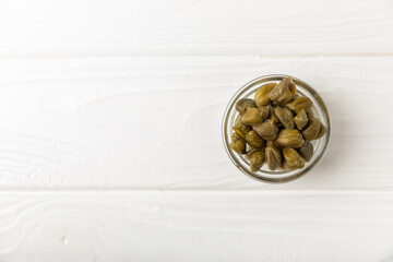 Capers in a bowl on a wooden kitchen table. Capers with sea salt and rosemary. Pickled capers.Mediterranean cuisine ingredient. Organic spices and seasonings. Copy space.