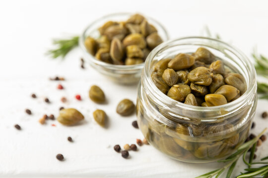 Capers in a bowl on a wooden kitchen table. Capers with sea salt and rosemary. Pickled capers.Mediterranean cuisine ingredient. Organic spices and seasonings. Copy space.