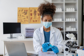 Young African female researcher in medical science laboratory with microscope analysis while doing...