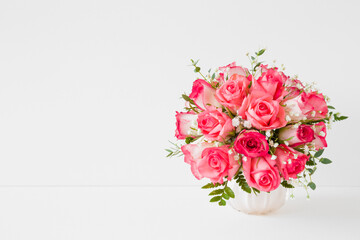 Beautiful wedding bouquet of fresh pink roses in vase on white table at light gray wall background. Empty place for inspirational, emotional, sentimental text, quote or sayings. Front view. Closeup.