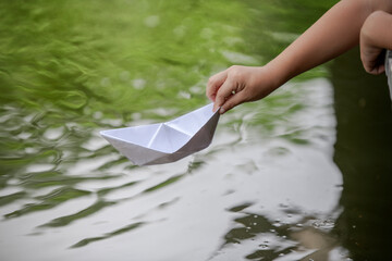 conceptual image of a child  hand release the paper boat into the lake