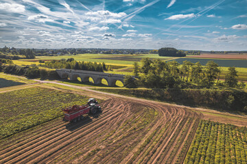 A sturdy tractor with a plow attached is hard at work tilling a vast field, with a rustic wooden...