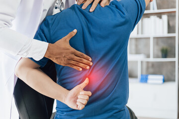 Doctor is diagnosing a patient's back pain in a hospital examination room. A male with back pain...