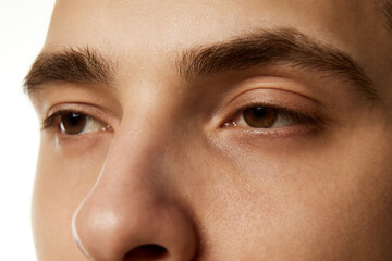 Close-up of male's face focusing on his eyes, eyebrows, and bridge of his nose against white studio...