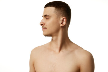 Profile view of brunette young handsome bearded man with bare shoulders against white studio background. Beautiful people. Concept of beauty procedures, male health, body care, spa treatment, hygiene.