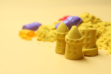 Castle figures made of yellow kinetic sand on beige background, closeup. Space for text