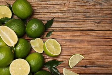 Fresh limes and green leaves on wooden table, flat lay. Space for text