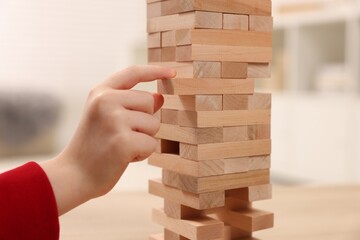 Child playing Jenga at table indoors, closeup