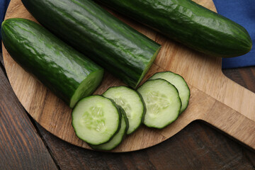 Fresh whole and cut cucumbers on wooden table, top view