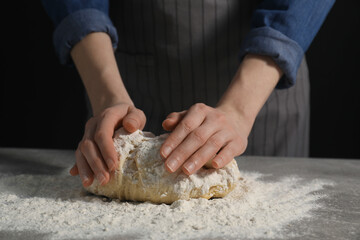 Making bread. Woman kneading dough at table on dark background, closeup