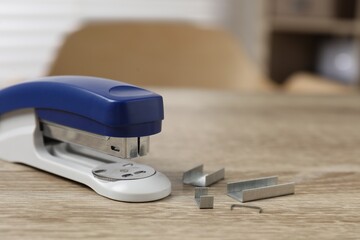 Bright stapler and metal staples on wooden table indoors, closeup