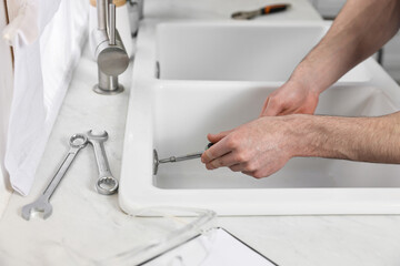 Plumber repairing sink with screwdriver indoors, closeup