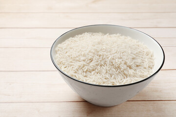 Raw basmati rice in bowl on white wooden table, space for text
