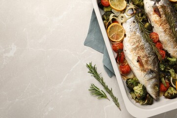Delicious fish with vegetables and lemon in baking dish on light marble table, top view. Space for...