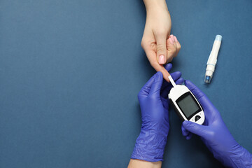 Diabetes. Doctor checking patient's blood sugar level with glucometer on blue background, top view....