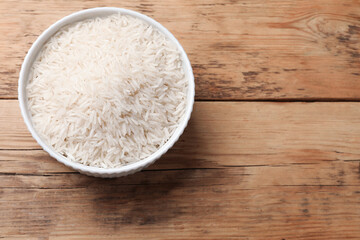 Raw basmati rice in bowl on wooden table, top view. Space for text