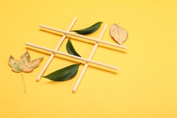 Tic tac toe game made with fresh and dry leaves on yellow background, space for text - obrazy, fototapety, plakaty
