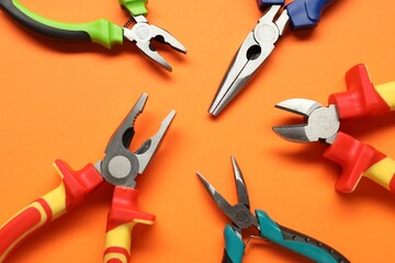 Different pliers on orange background, flat lay