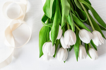 fresh bouquet of white tulips with lush green leaves on white textured surface, Mothers day or Women's day. Top view with copy space Floral composition Romantic background - 746608100