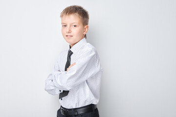 Confident young boy in a white shirt and tie, standing with arms crossed against a plain background