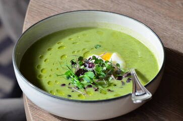 GREEN FRESH PEA ASPARAGUS CREAM SOUP SERVED ON WOODEN TABLE IN RESTAURANT, HEALTHY FOOD BACKGROUND, CLOSE VIEW