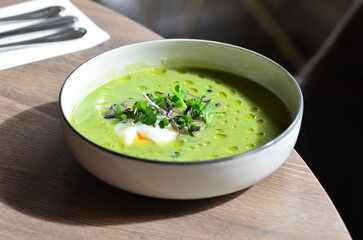 GREEN FRESH PEA ASPARAGUS CREAM SOUP SERVED ON WOODEN TABLE IN RESTAURANT, HEALTHY FOOD BACKGROUND, CLOSE VIEW