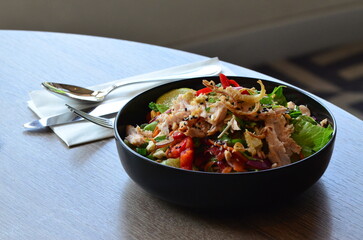 beautiful asian salad with chicken, served in a black bowl, in a restaurant
