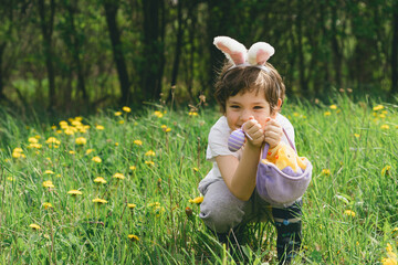 Funny boy with eggs basket and bunny ears on Easter egg hunt in sunny spring garden. Hunting for Easter eggs