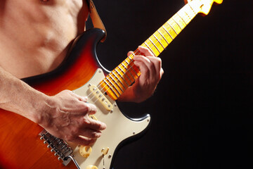 Rock guitarist playing the sunburst electric guitar on dark stage.
