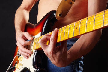 Artist playing the sunburst electric guitar on dark stage.