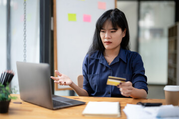 Stressed Asian businesswoman looking at laptop screen while holding credit card and facing transaction problems