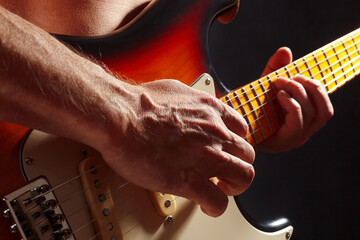 Hands of rock musician playing the sunburst guitar on dark stage.