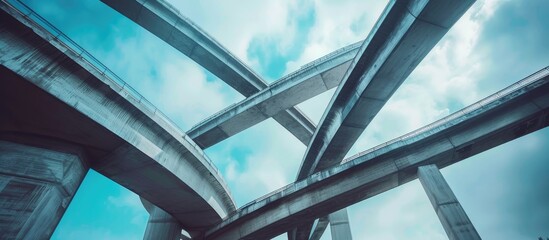 A modern multilevel road junction, showcasing the intricate design and construction of the bridge from a ground-level perspective. The bridge spans overhead, revealing the structural elements and