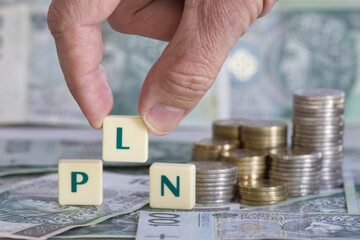 A hand composes the inscription PLN on plastic blocks. PLN is the abbreviation for Polish zloty,...