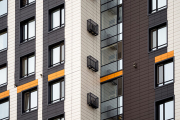 Fragment of a multi-storey house with windows, balconies, insulated ventilated facades and decorative boxes for air conditioners. Construction industry.