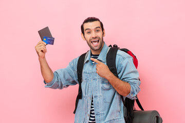 Smiling solo tourist man backpacker pointing to passport and credit card in his hand on pink color...
